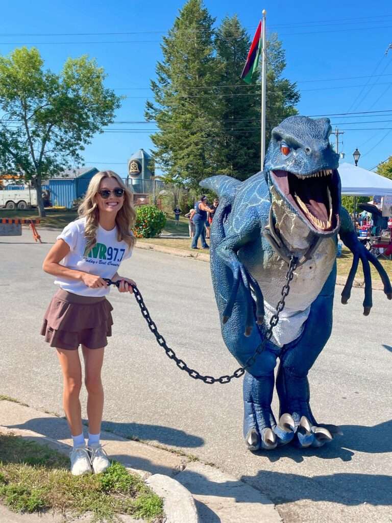 Radio host Sophie from AVR 97.7 & Magic 94.9 poses with a roaring T-Rex at the Windsor waterfront during the Avon River Days Kids Carnival in Nova Scotia.